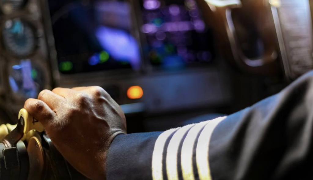 Airline pilot, captain, in flight deck with hand on throttle - bizav pilot shortage